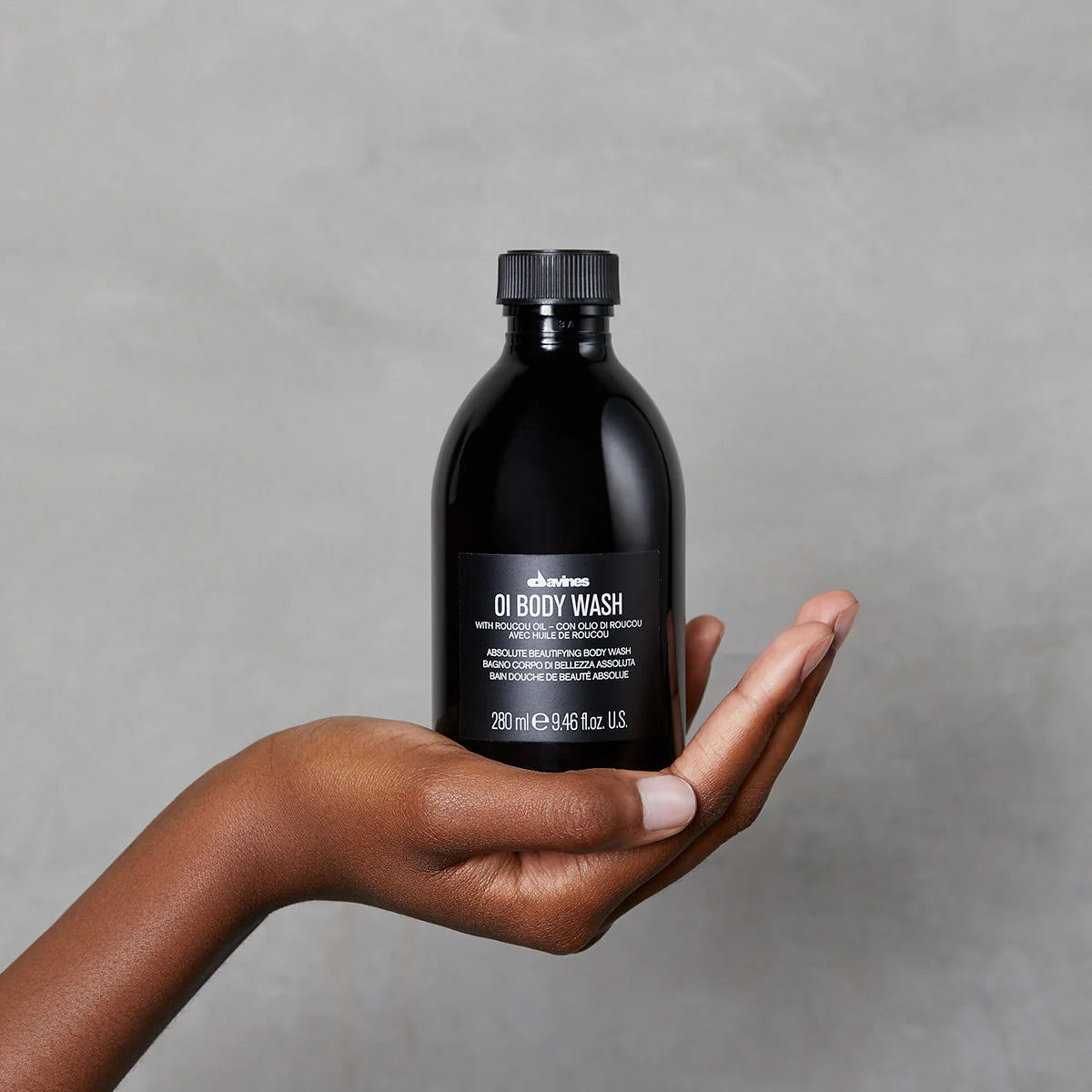 Hand holding a black bottle of OI Body Wash against a gray background