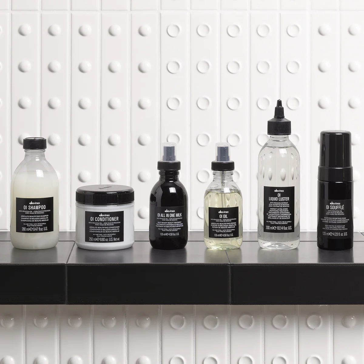 Collection of Davines OI hair care line on a shelf with a white tiled wall background