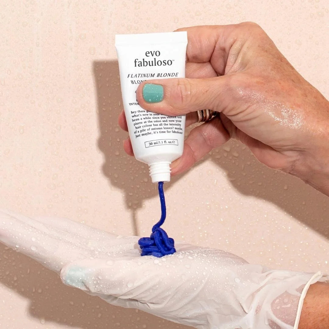 Hand holding a tube of evo fabuloso hair color with blue product on a beige background