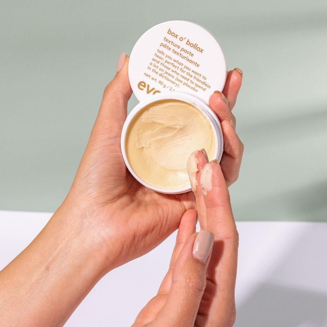 Hand holding a container of texture paste with a neutral background