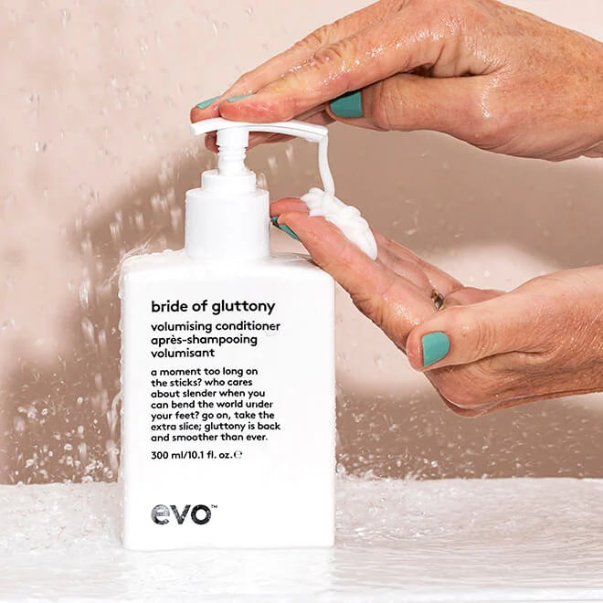 Bottle of EVO 'bride of gluttony' volumising conditioner with hands squeezing it.