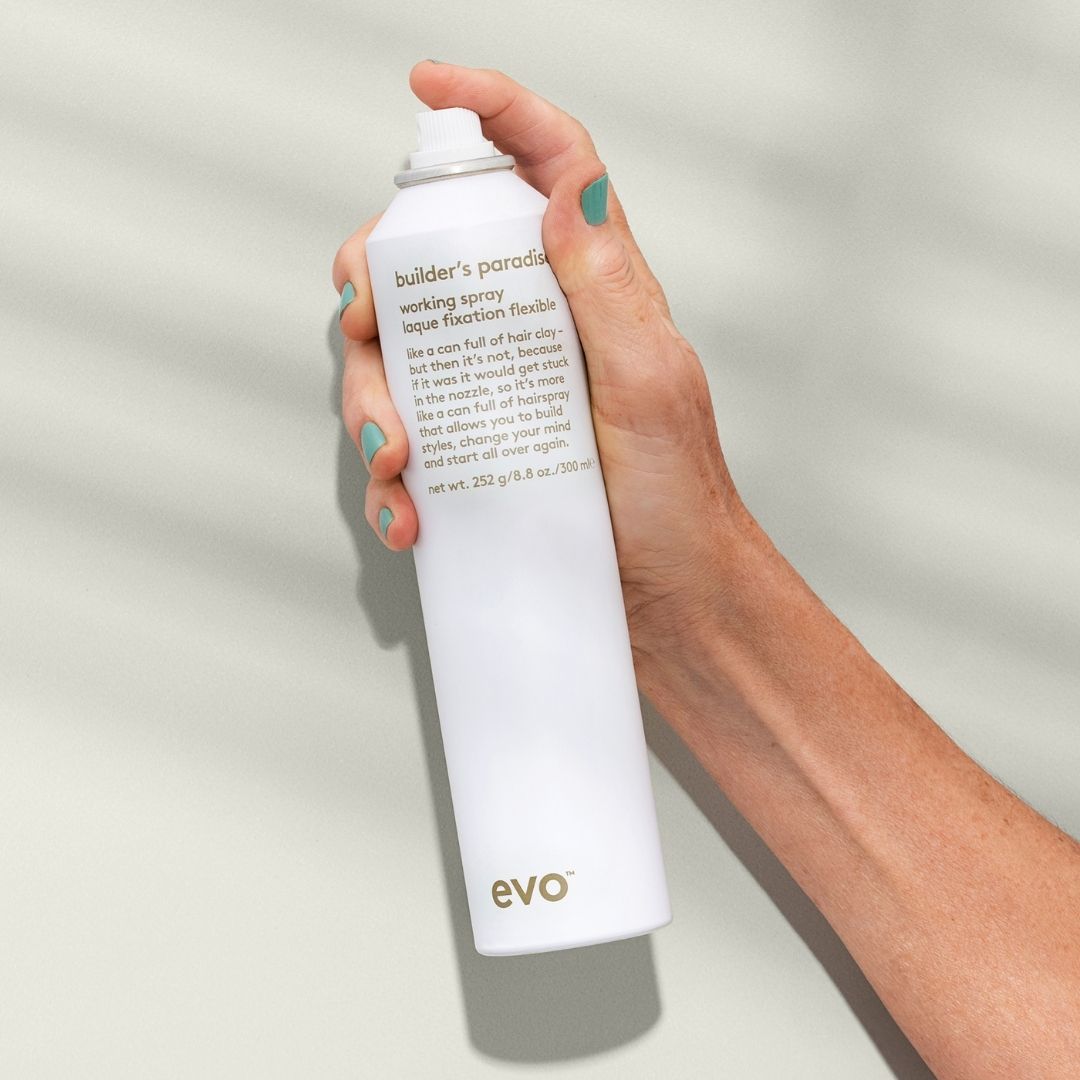 Hand holding a white spray bottle labeled 'evo' against a light background