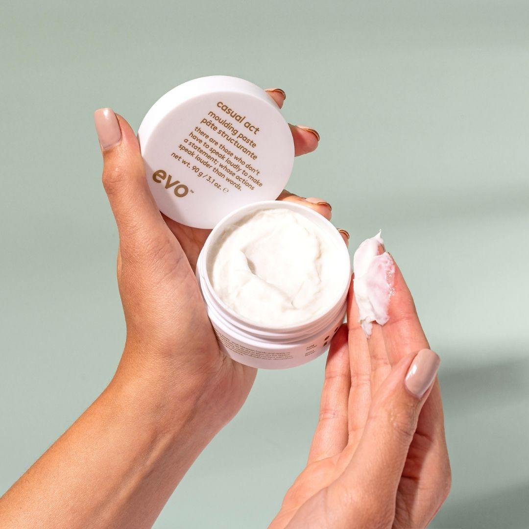 Person holding a jar of evo makeup product with a light green background