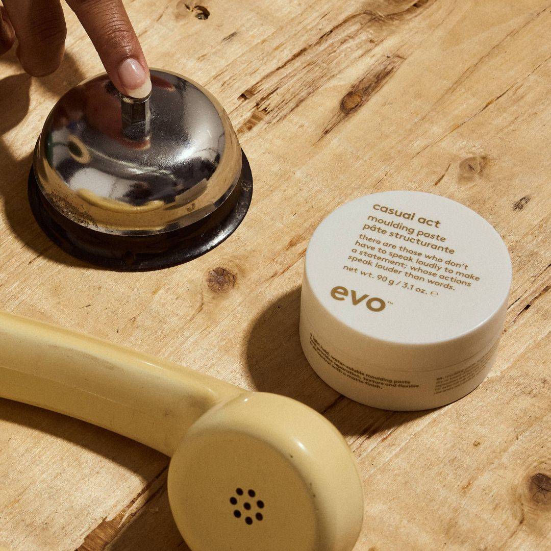 Hand ringing a bell on a wooden surface with a jar of 'evo' product nearby.