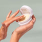 Hand holding a white jar of crop strutters construction cream with a green background