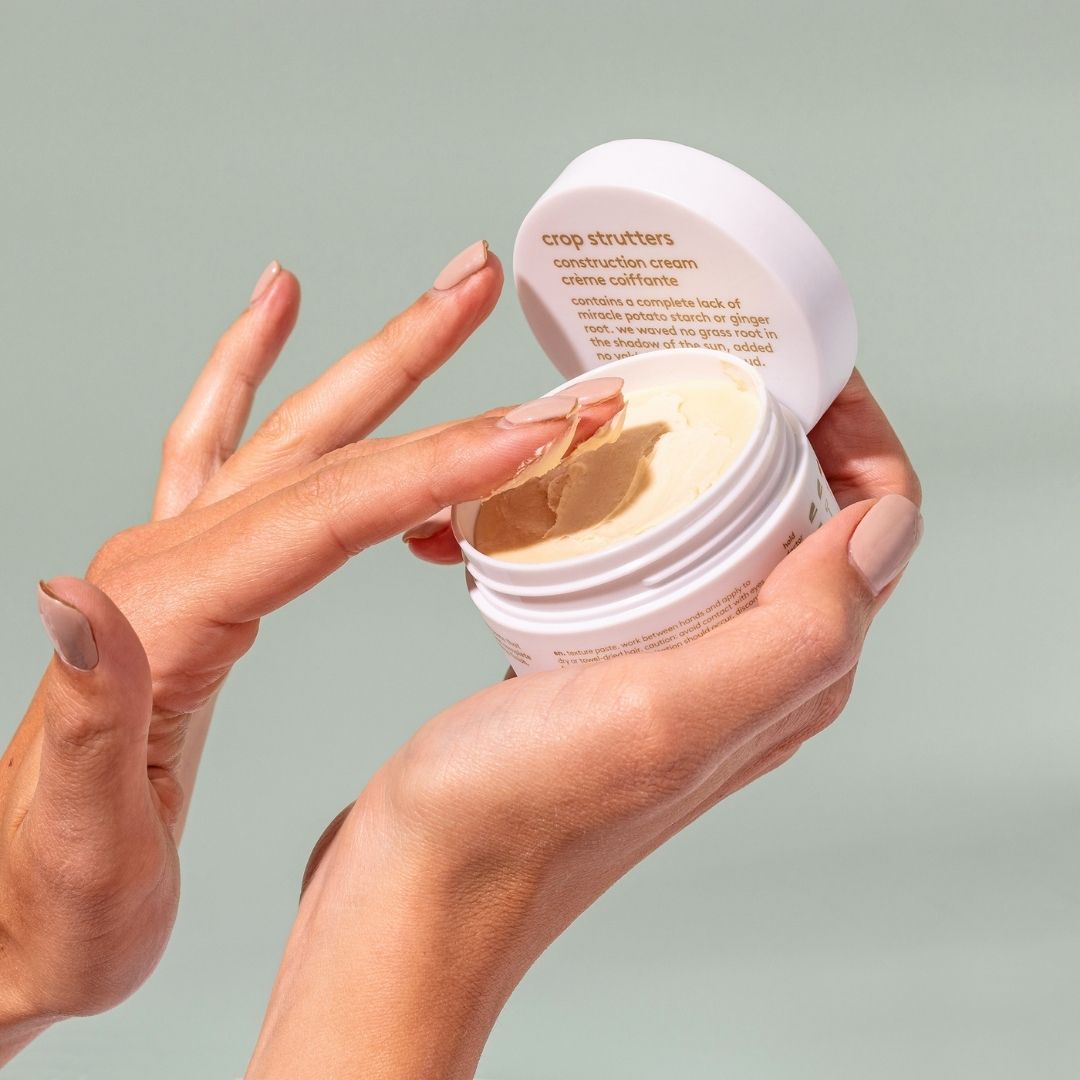 Hand holding a white jar of crop strutters construction cream with a green background