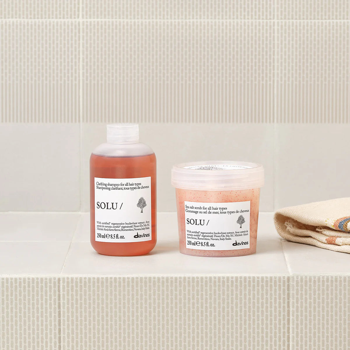 Two bottles of Davines SOLU hair care products on a bathroom shelf with a towel
