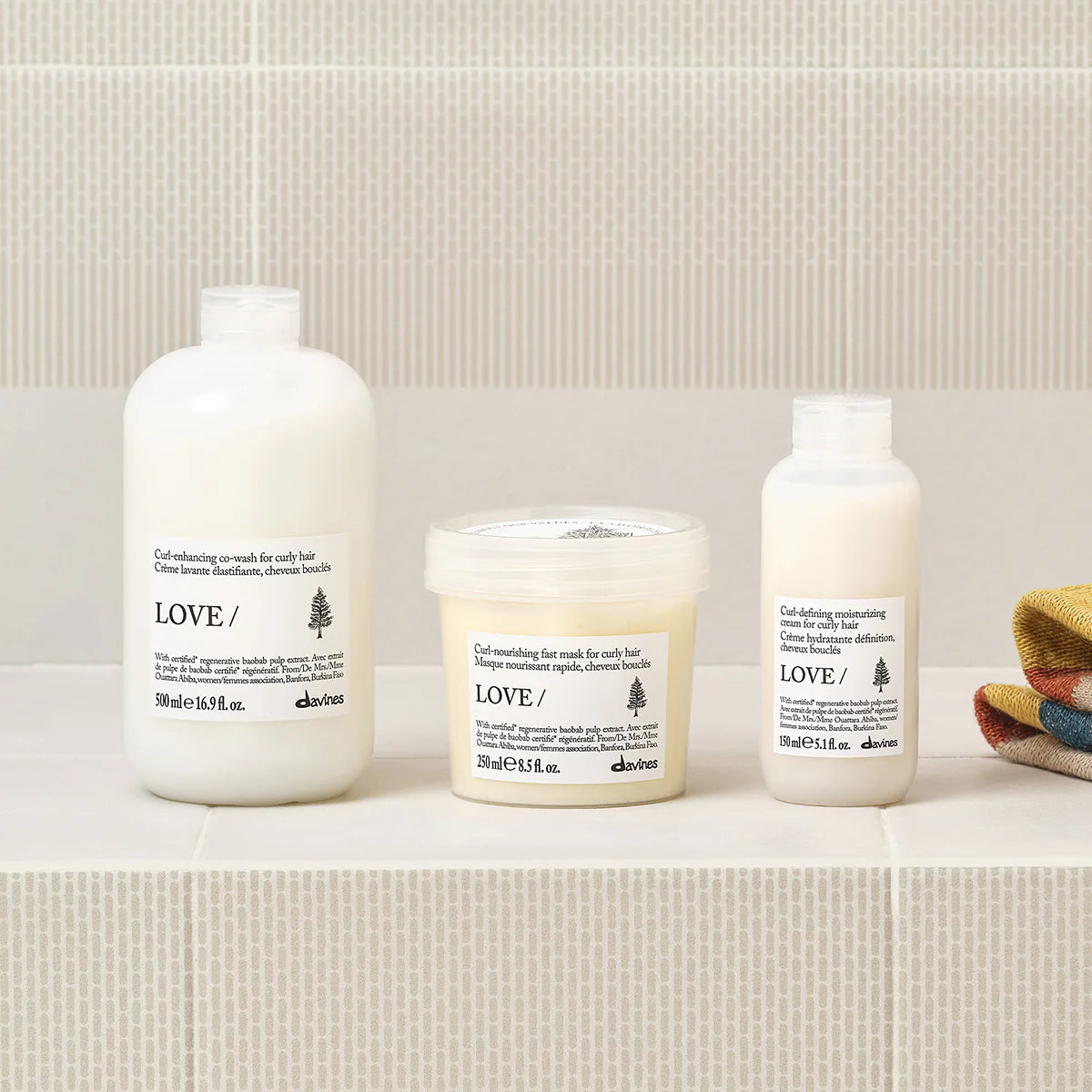 Three Davines hair care products on a bathroom shelf with a tiled wall background