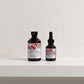 Two bottles of shampoo and serum on a white surface with a geometric tile pattern.