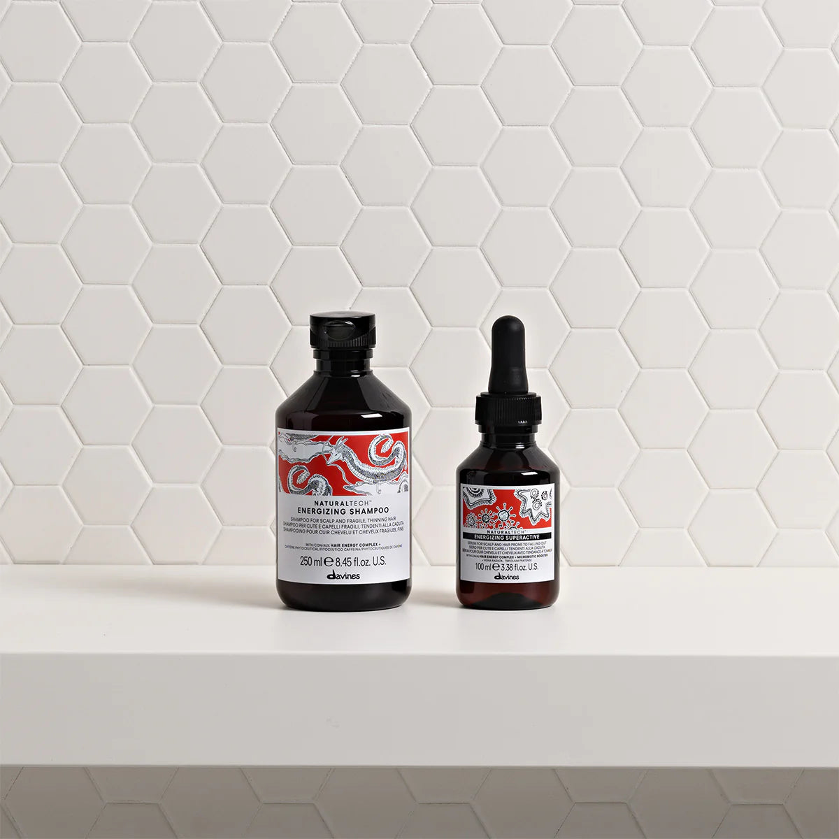 Two bottles of shampoo and serum on a white surface with a geometric tile pattern.