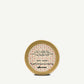 Gold container of glossy styling wax with decorative lid and text on a white background