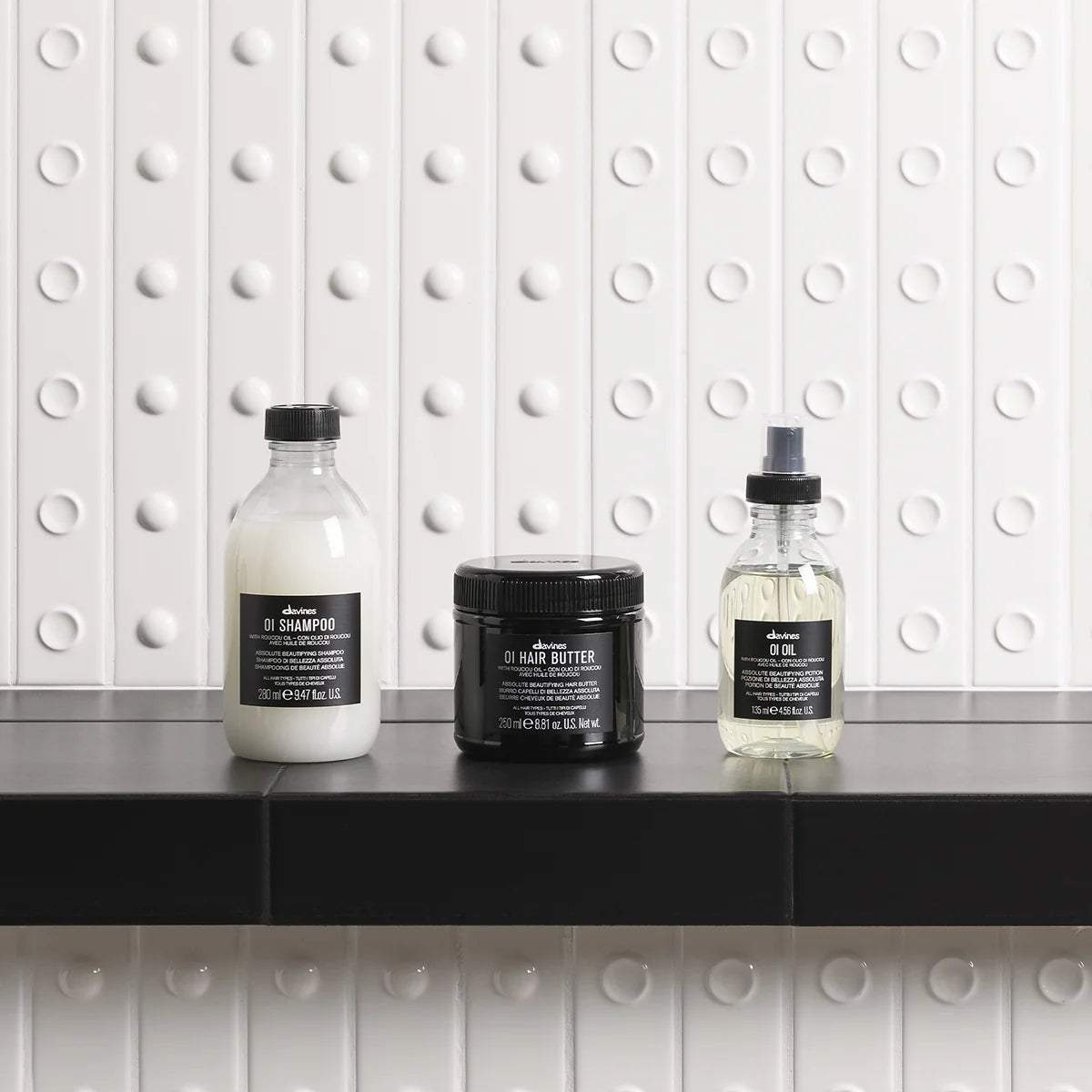 Three Davines hair care products on a black surface with a white tiled wall background