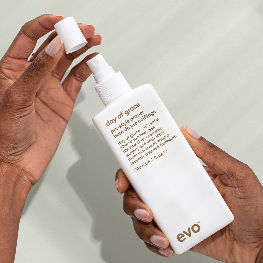 Person holding a bottle of 'day of grace' pre-style primer by evo against a neutral background