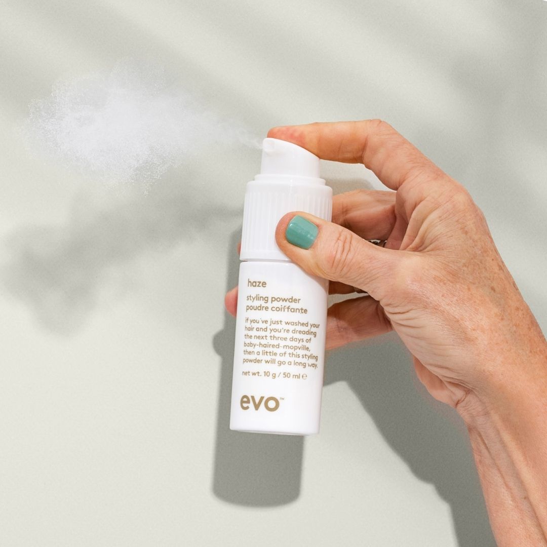 Hand holding a bottle of evo styling powder against a neutral background