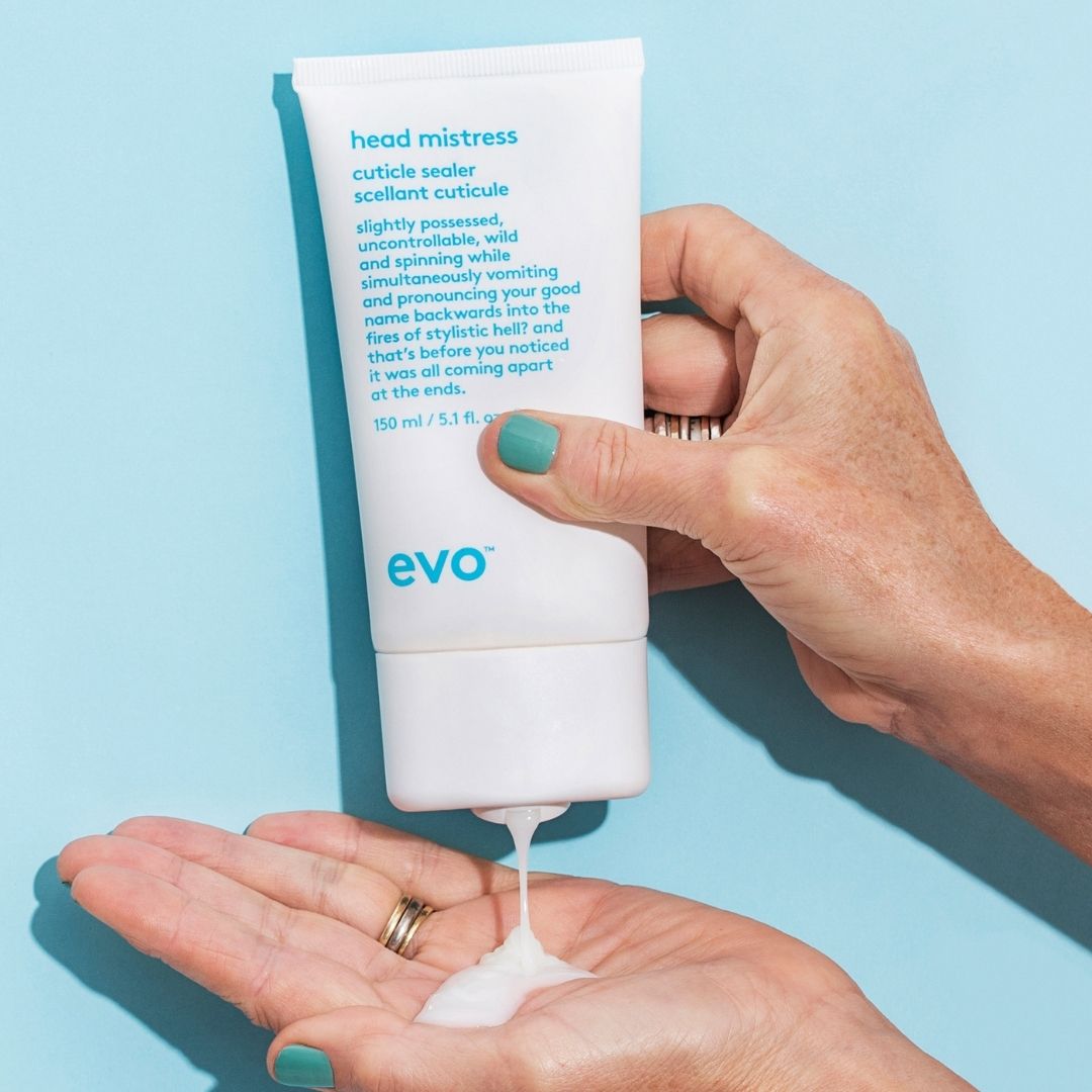Right hand squeezing Head Mistress Cuticle Sealer into left hand against blue background