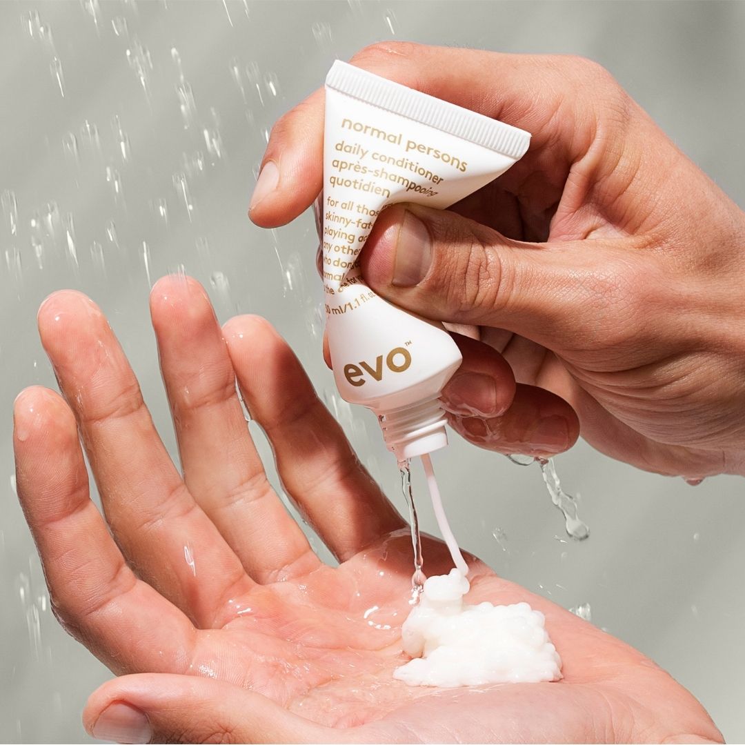 Hand holding a small bottle of evo product over another hand with visible liquid being poured.