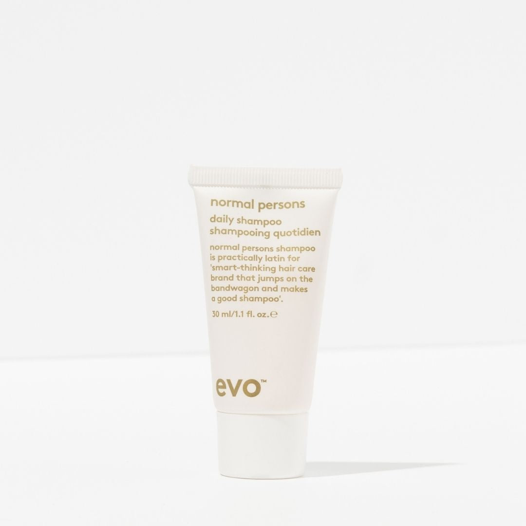 Small white container of 'normal persons' shampoo with gold text on a white background