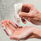Person holding a tube of evo shampoo over soapy hands with water droplets in the background
