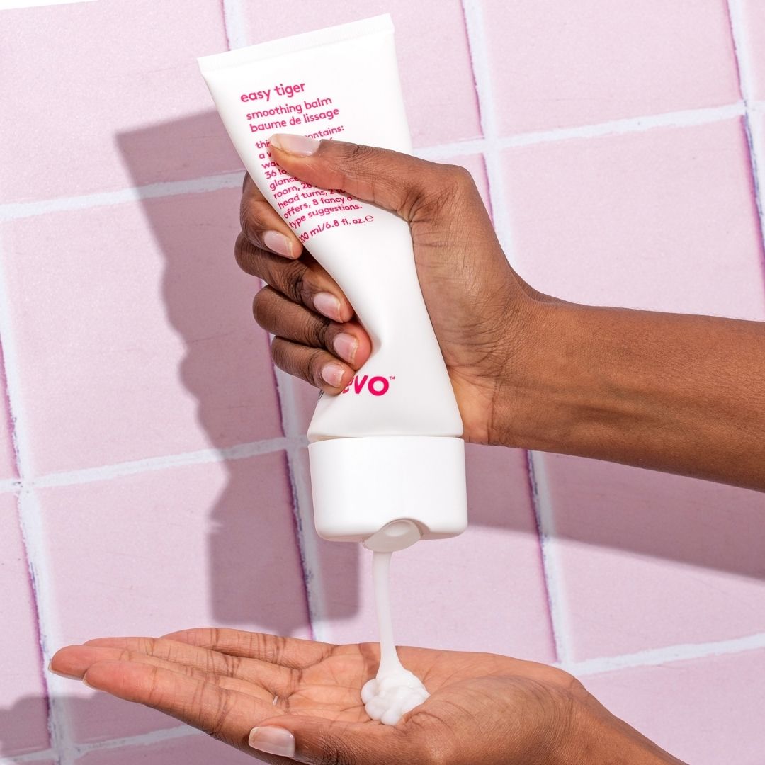 Hand holding a tube of 'easy tiger' balm with a pink background