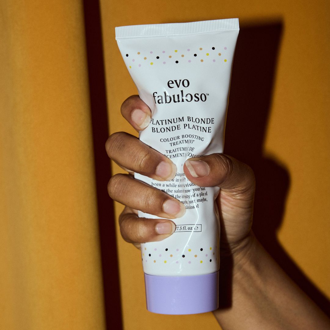Hand holding a tube of evo fabuloso platinum blonde hair treatment against an orange background