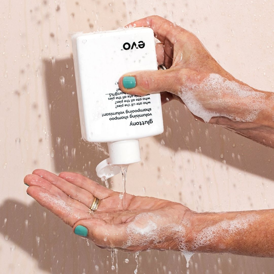 Person holding a white bottle labeled 'EVO' with soap being dispensed into hands against a beige background.