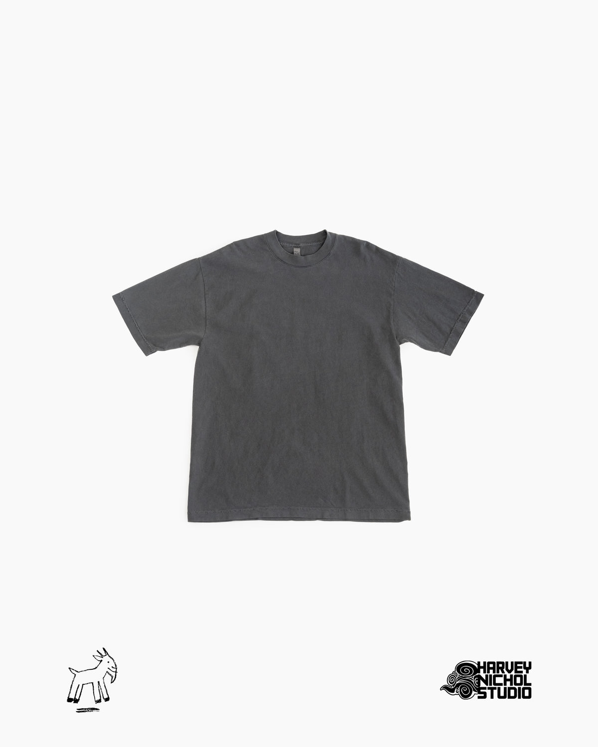 Front of dark grey t-shirt against white background; GOAT logo in lower left corner, Harvey Nichol Studio logo in lower right corner
