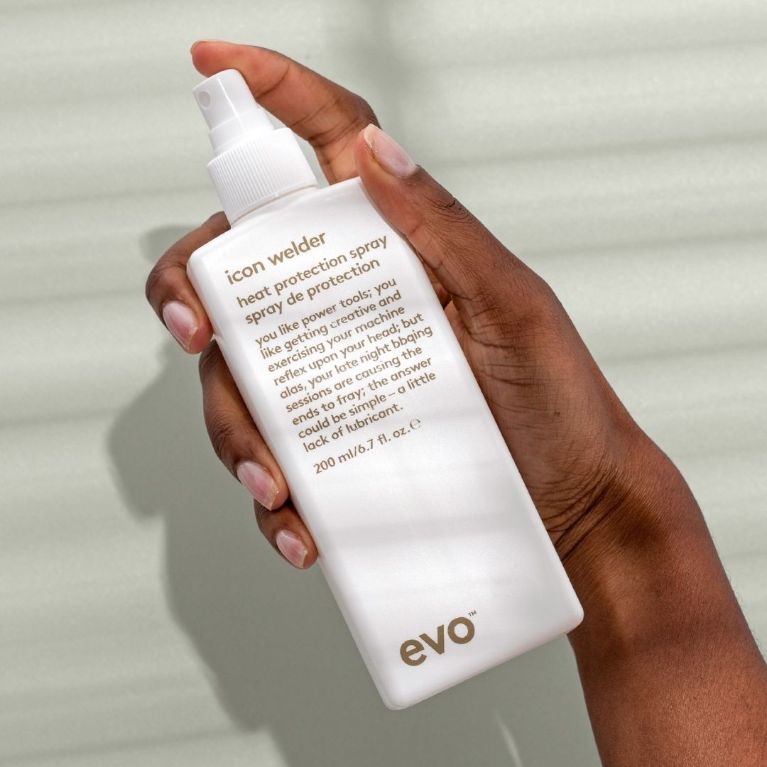 Hand holding a bottle of evo icon welder heat protection spray against a neutral background