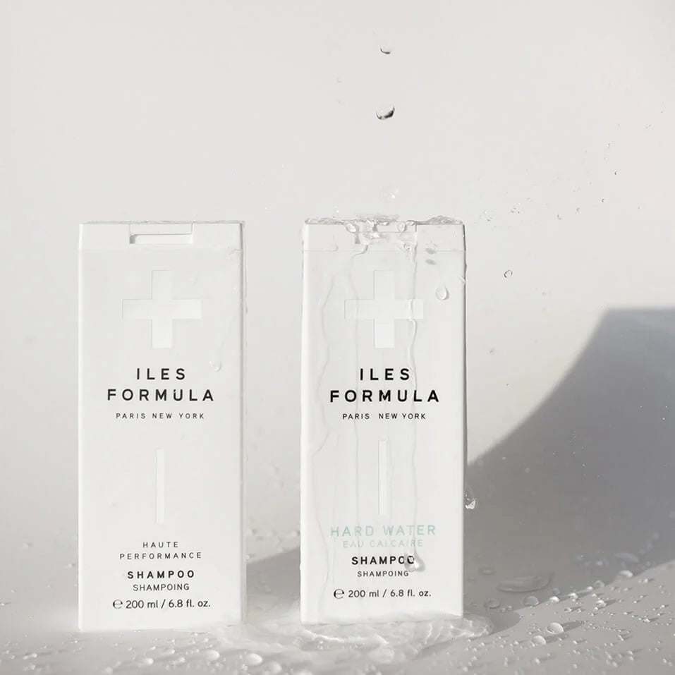Two bottles of Iles Formula shampoo on a textured white surface.