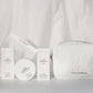 Iles Formula haircare products and a white vegan leather cosmetic bag with a white flowy fabric background