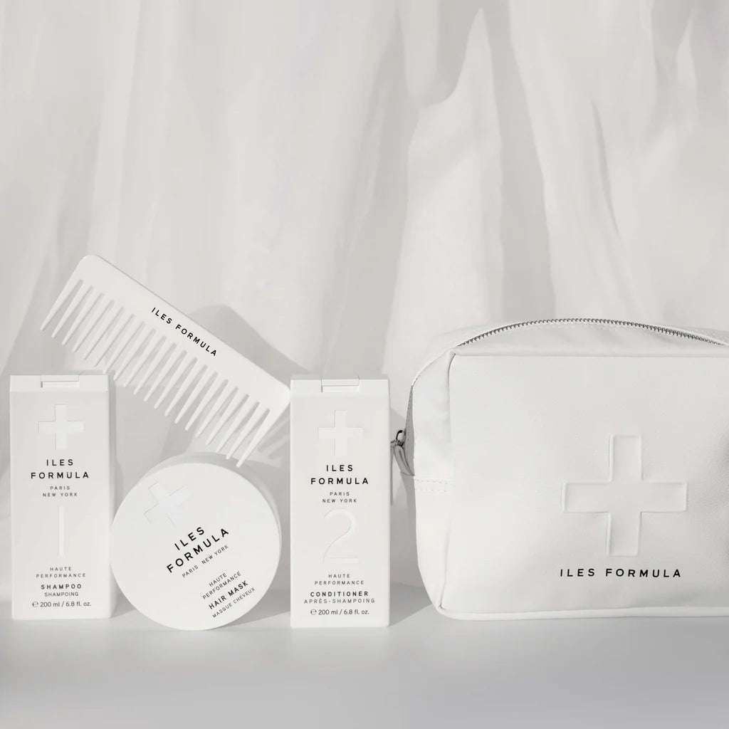 Iles Formula haircare products and a white vegan leather cosmetic bag with a white flowy fabric background