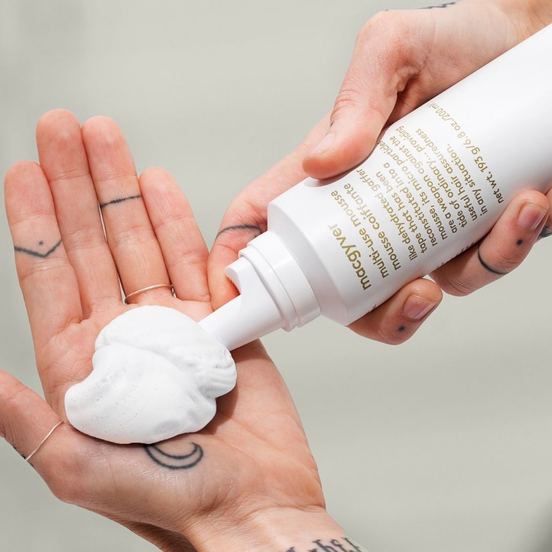 Person holding a white bottle with a pump, applying cream to their palm against a neutral background