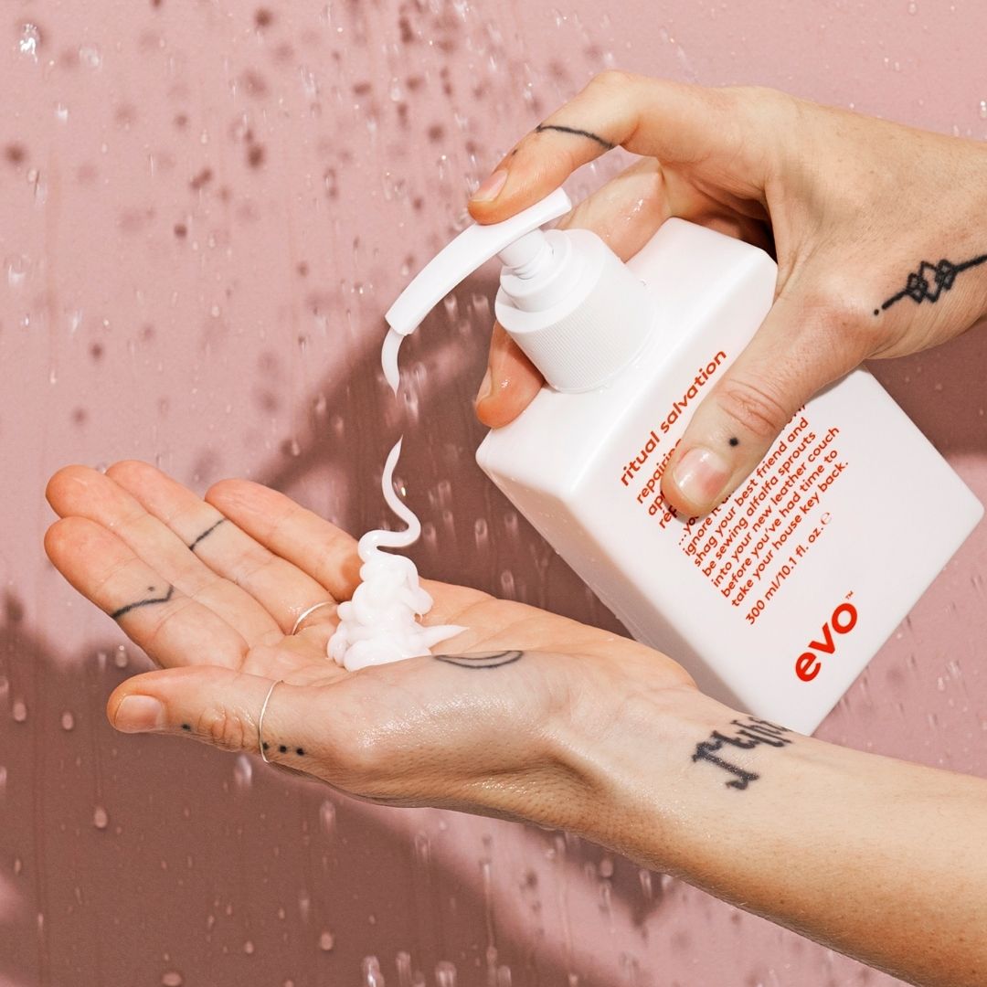 Person applying evo ritual salvation cream to their hand against a pink background