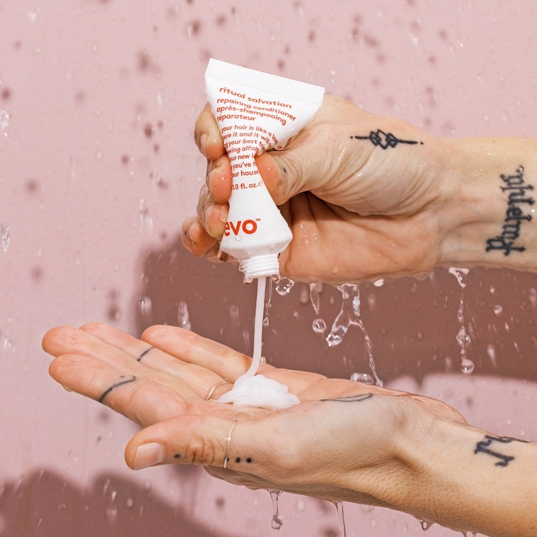 Hand applying a white cream from a tube labeled 'EVO' against a pink background
