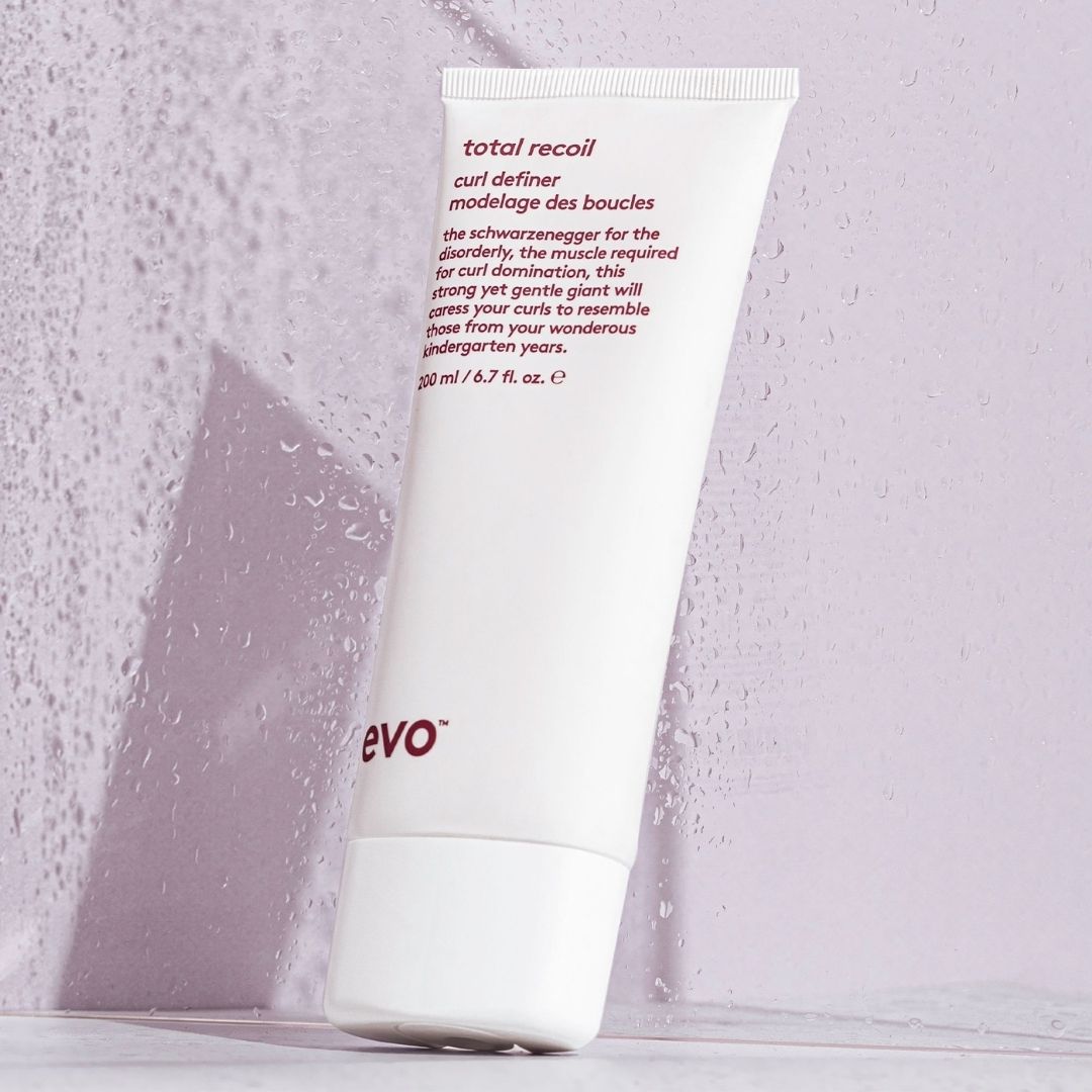 White tube of 'total recoil' hair product with purple text on a textured light gray background
