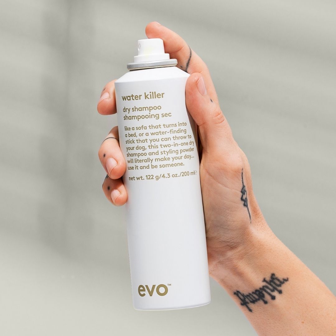 Hand holding a bottle of evo water killer dry shampoo against a neutral background
