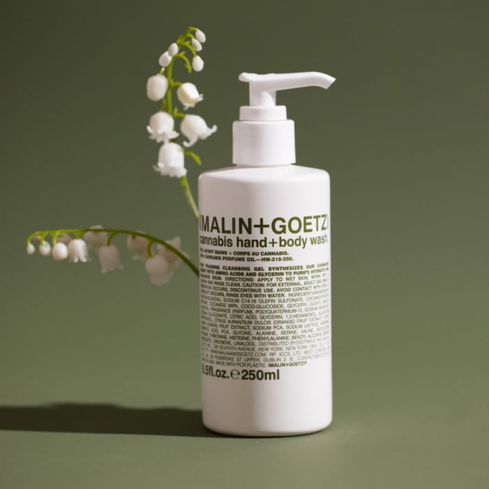 Malin+Goetz cannabis hand and body wash bottle with a branch of white flowers on a green background
