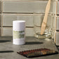 Malin+Goetz deodorant stick on a bathroom counter with a glass and comb.