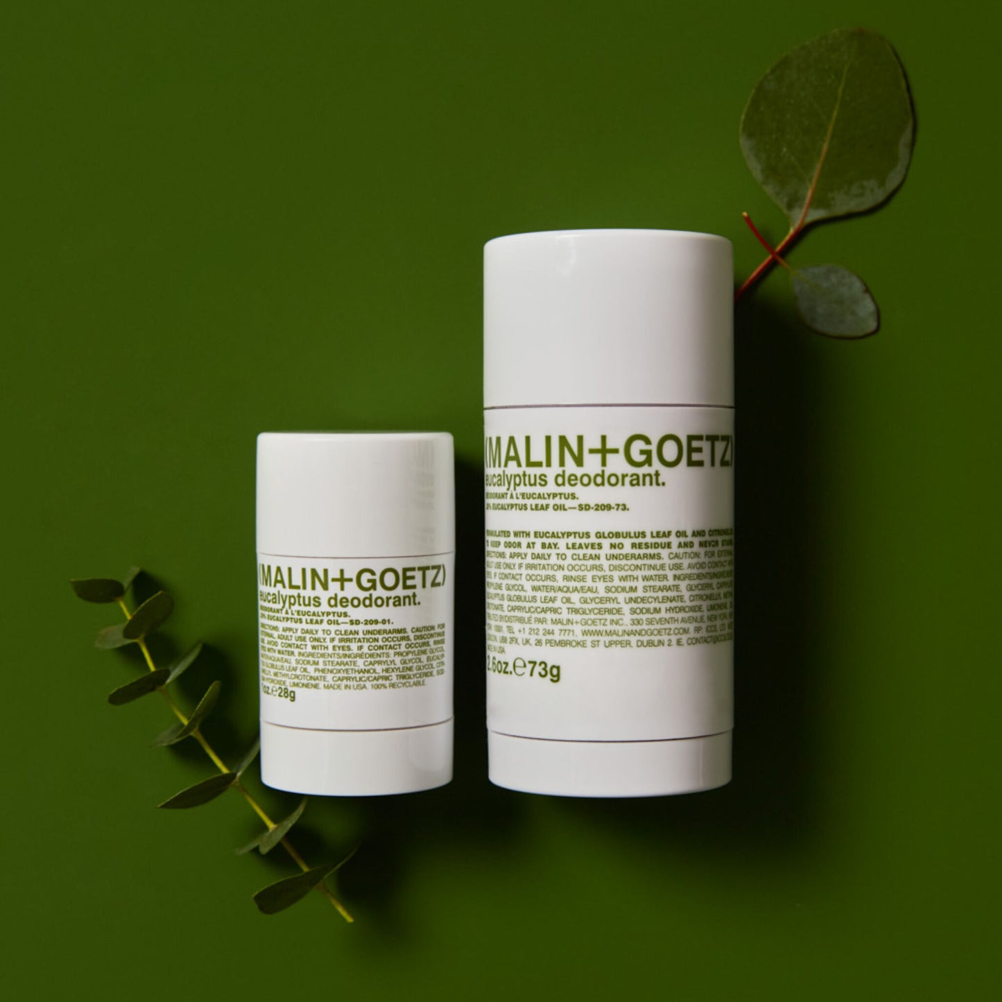 Two Malin+Goetz deodorant containers on a green background with leaves.