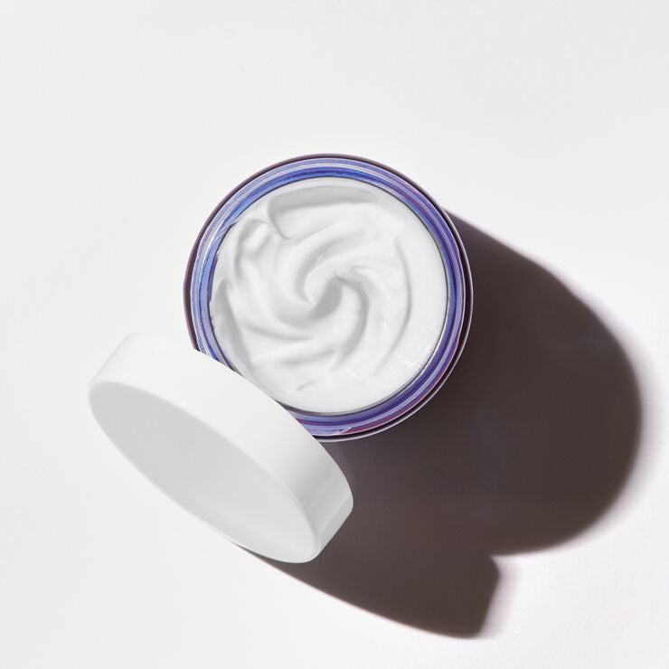 Open jar of white cream with a swirled top on a light gray background