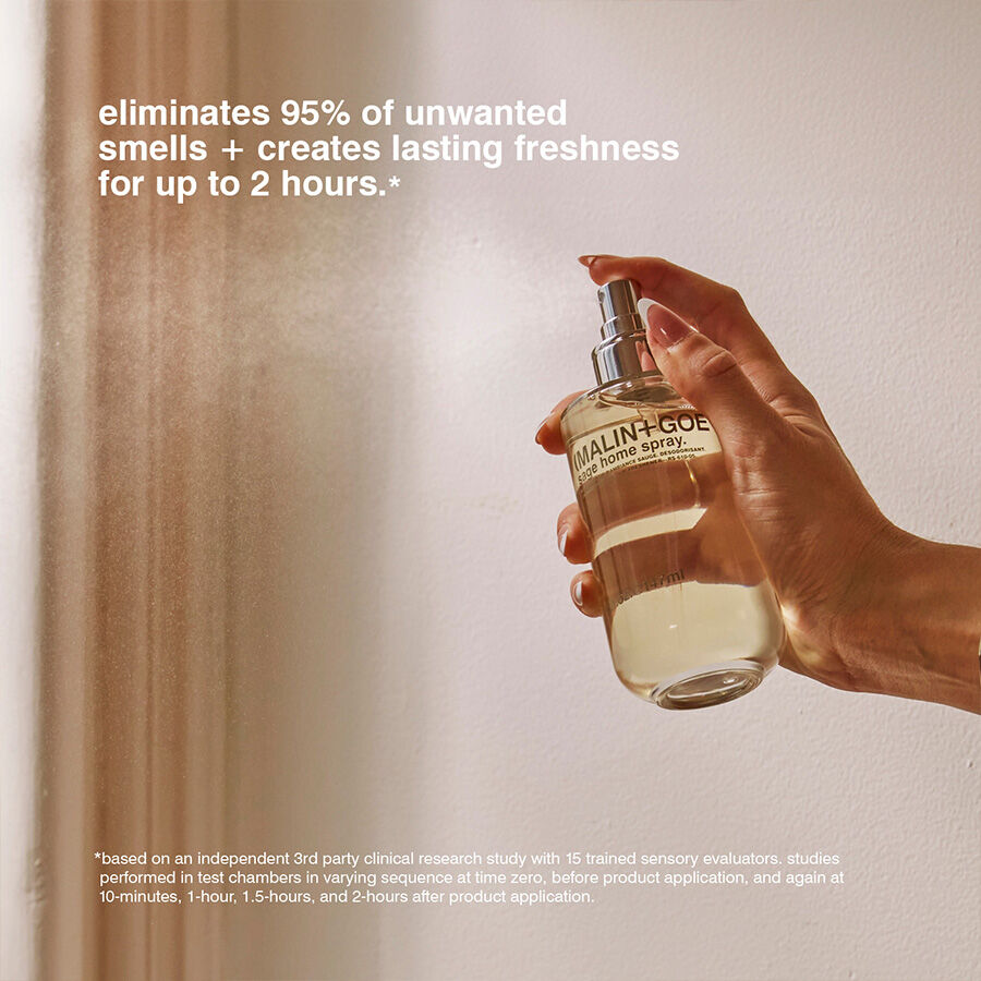 Hand holding a bottle of Malin+Goetz room spray with text about its smell-eliminating properties.