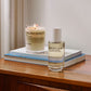 Malin+Goetz candle and home spray on a wooden surface with books