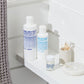 MALIN+GOETZ skincare products on a bathroom shelf with a towel and toothbrush holder.