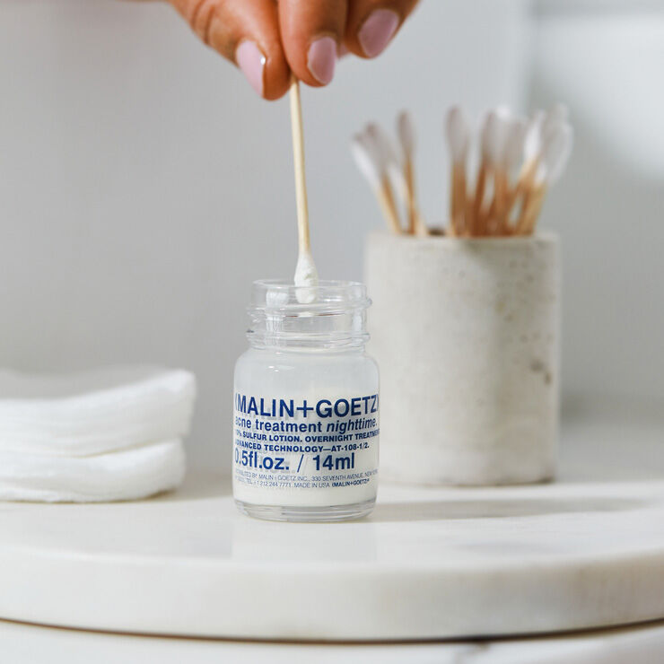 MALIN+GOETZ skincare product with a dropper on a marble surface.