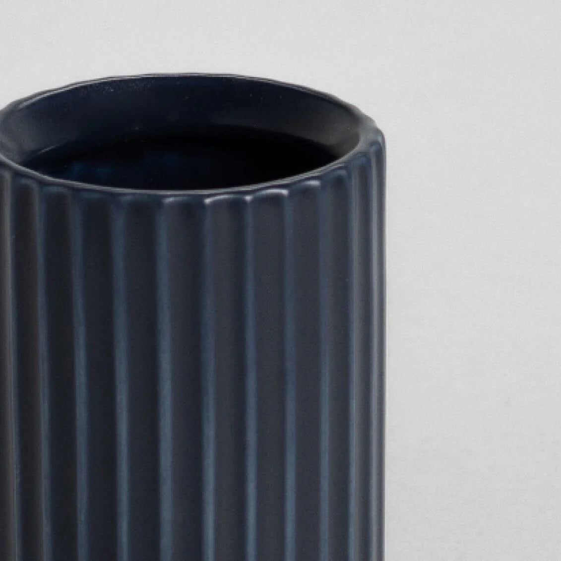 Dark blue cylindrical vase with ribbed texture on a light gray background
