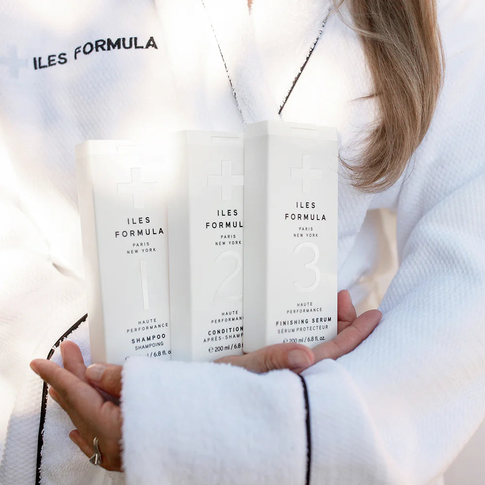 Three bottles of ILES FORMULA products held by a person wearing a white robe.